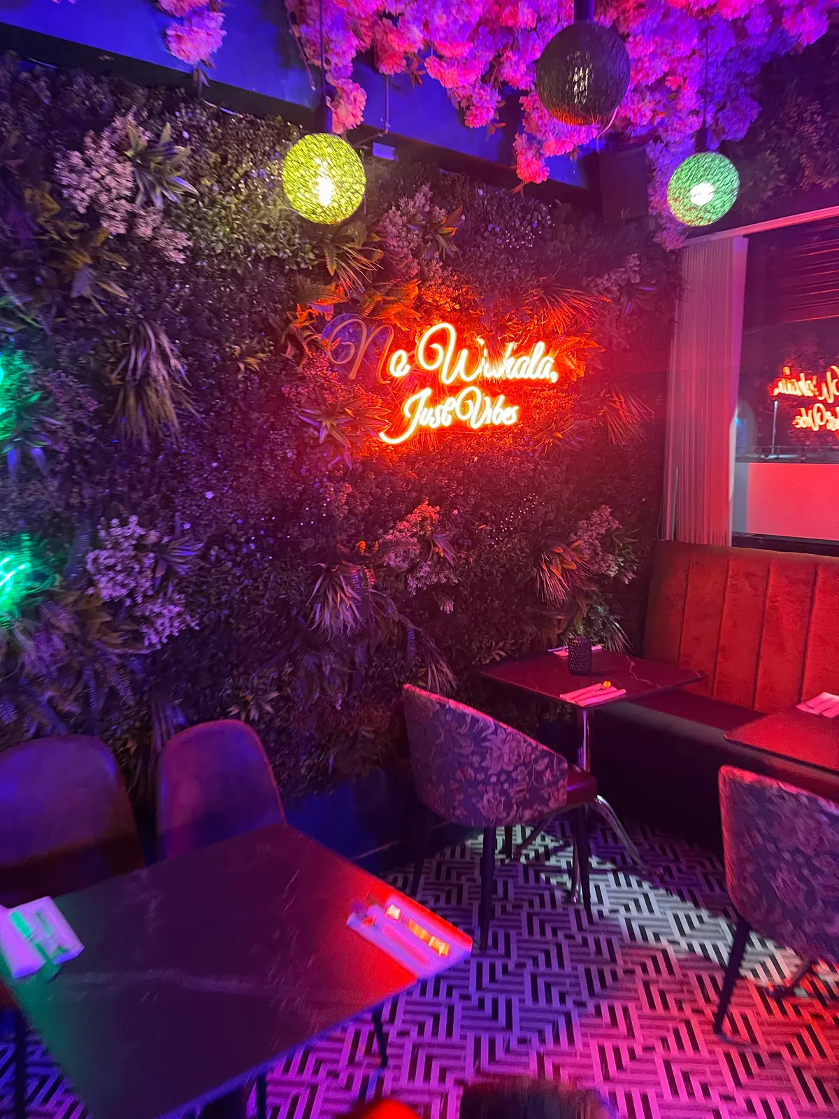 ESQ seating beneath the No Wahala Just Vibes neon sign and floral ceiling